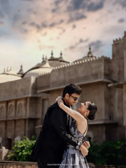 An intimate embrace between the couple with the grand facade of Six Senses Fort Barwara against a dramatic sky.