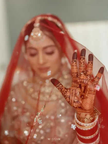 A powerful close-up of a Punjabi bride's hand, showcasing her beautiful red 'chura' and intricate mehendi. The focus on her hand, with the ring and veil, symbolizes the promises and traditions of her wedding day.