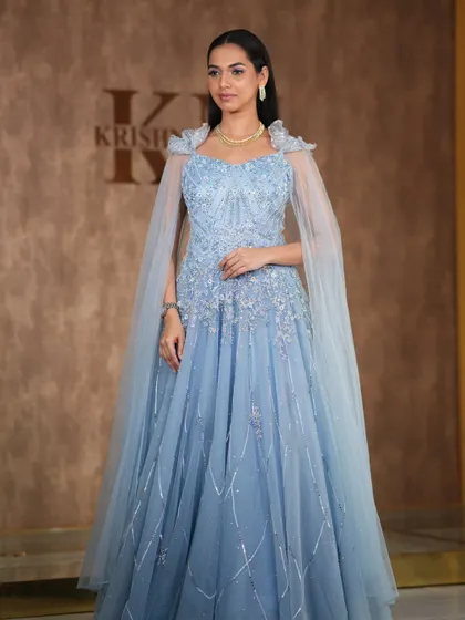 A fairytale moment in this powder blue gown with a sheer cape. The simple diamond necklace adds a touch of elegance, making it perfect for a reception or pre-wedding photoshoot.