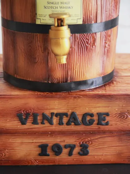 The base of the barrel cake was designed to look like a rustic wooden crate, complete with a "Vintage 1973" inscription.