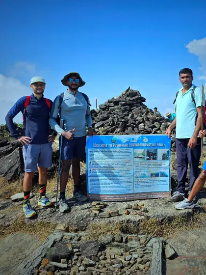 Trekkers at the Pushpagiri (Kumaraparvatha) peak, standing by the official board that marks the summit.