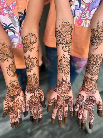 Four hands together, each adorned with a unique and beautiful floral henna design. This is a perfect example of a coordinated look for a group of bridesmaids or friends.