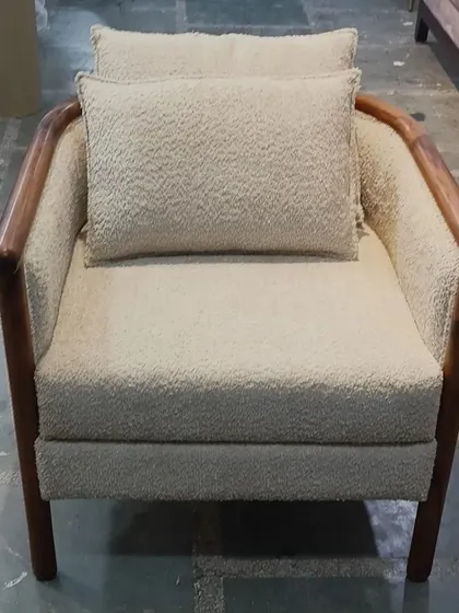 A full shot of our minimalist armchair with a wooden frame and bouclé upholstery, pictured in our workshop. This highlights the raw beauty and solid construction of the piece before it is placed in a finished interior.
