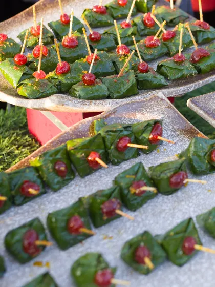 A beautiful display of our sweet paan. Each betel leaf is carefully folded and topped with a candied cherry, arranged on platters for guests to enjoy as a post-meal digestive and mouth freshener.