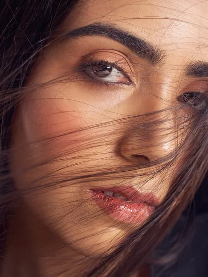 An intimate portrait where the focus is on texture and light. The skin has a beautiful, natural sheen, and the lips have a soft, glossy finish, creating a look that is both raw and refined.