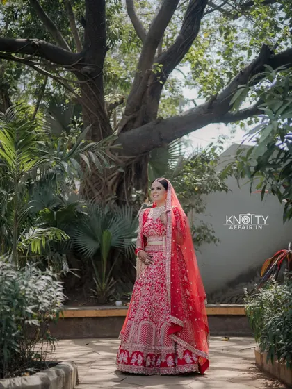 A full-length portrait of the bride in her red lehenga, standing in a beautiful garden. We showcase the entire bridal look from head to toe.