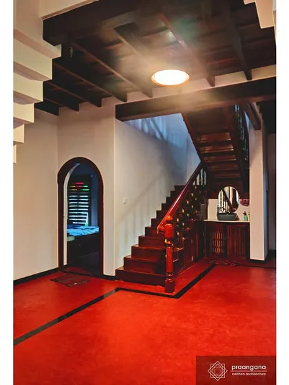 The vibrant red oxide flooring of the entrance hall leads to a beautifully crafted wooden staircase. The contrast with the white lime-washed walls is a hallmark of this style.