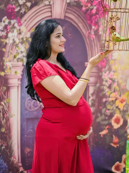 A fairytale theme in an outdoor setting. The mom-to-be in her red dress with a prop birdcage looks like she's stepped out of a story.