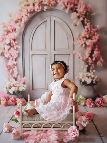 What a happy smile! This little girl is enjoying her sitter session in a lovely floral setup with a miniature bed prop.