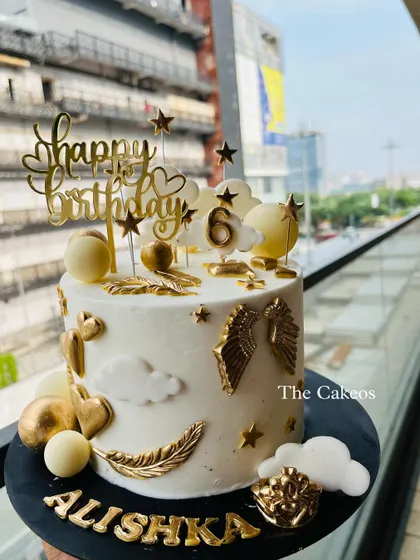 An elegant and heavenly angel-themed cake. This white and gold design features golden wings, feathers, clouds, and stars, creating a celestial look for a special birthday.