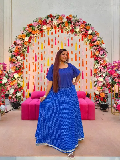 Dressed in a vibrant blue lehenga for a Mehendi ceremony, standing before a beautiful floral arch. My outfits are always chosen to complement the festive decor and add to the colorful atmosphere of the event.