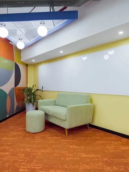 A small, informal meeting nook designed for quick brainstorming sessions. The colorful wall mural, comfortable loveseat, and large whiteboard make it a functional and inspiring corner of the office.