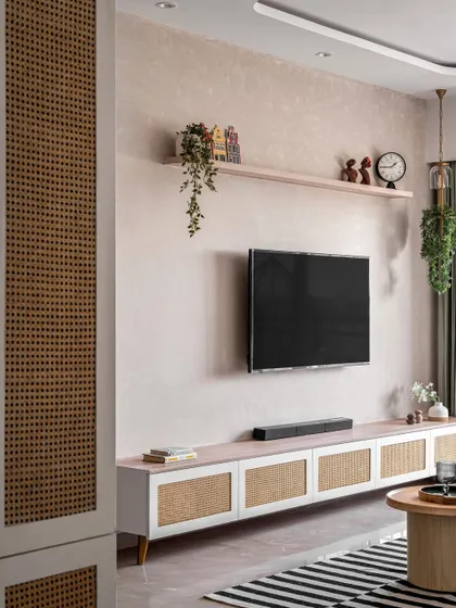 This TV unit combines a textured wall with a low-profile console featuring rattan cabinet doors. The design is clean and modern, with a floating shelf for displaying personal decor items.