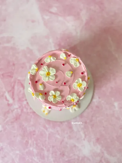 An overhead view of the pink mini cake, covered in delicate, hand-piped white daisies. The simple, clean design is both pretty and elegant.