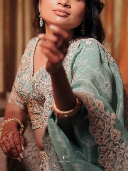 A close-up shot of the bride's hands and intricately embroidered lehenga during her engagement. The details of the attire are an important part of the story.
