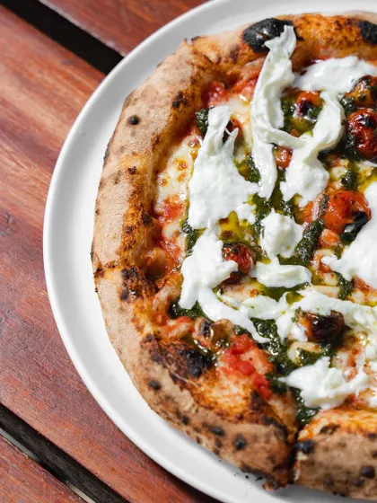 A top-down view of the Stracciatella Pizza, showcasing the generous amount of fresh cheese and pesto drizzled over the top.