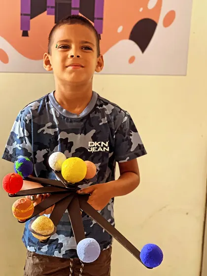 This student proudly displays the complete solar system model he built during our space-themed workshop.