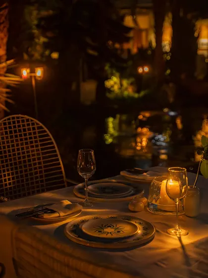 A romantic, candlelit table for two set by the water at night. This image is all about selling an experience, creating a mood of intimacy and special occasion for a fine-dining restaurant.