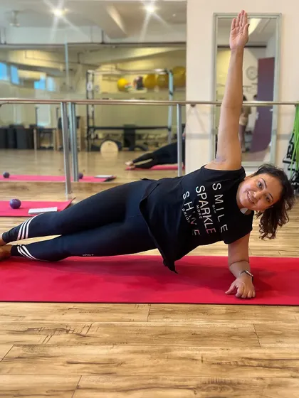 A member holds a strong side plank on the mat, smiling, showing that building strength can be a joyful process.