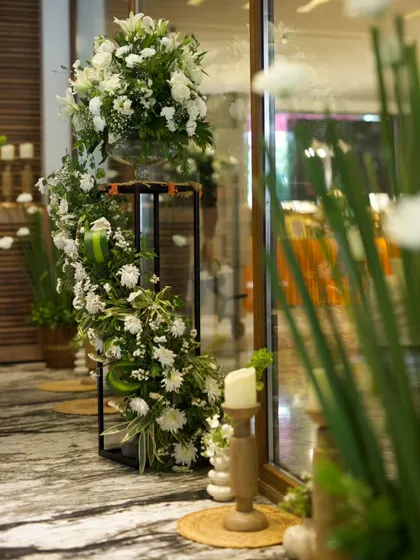 Elegant floral stands for a Roka ceremony. Cascading white flowers on black metal stands, paired with wooden candle holders, create a sophisticated and welcoming entrance.