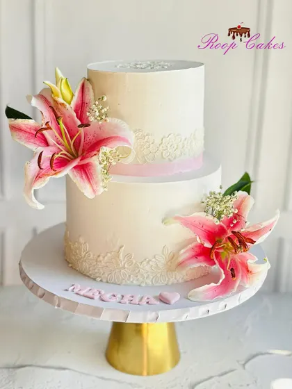 Isn't it gorgeous? This stunning two-tier cake combines a delicate lace stencil with the vibrant beauty of fresh pink lilies.