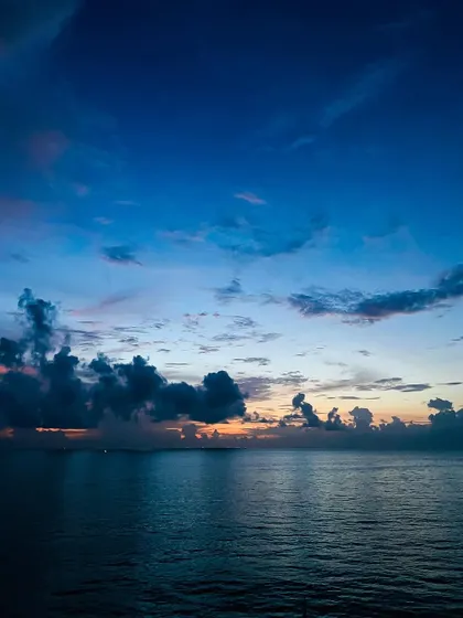 A breathtaking sunset over the open ocean, as seen from the deck of a cruise ship. The deep blues and subtle oranges create a serene and powerful seascape.