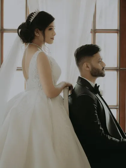 A stylish, editorial-style portrait of the bride and groom, posed back-to-back by a window.