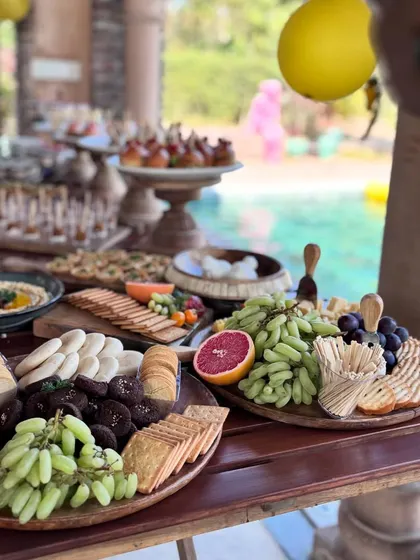 An abundant grazing table set for a sun-drenched poolside party. I customize each spread to match the event's theme, featuring a vibrant mix of fresh fruits, artisanal cheeses, crackers, and gourmet bites.