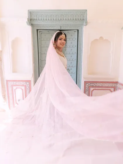 A dreamy bridal portrait, with the bride's light pink veil flowing in the air, creating a soft and ethereal effect against the pale blue door.