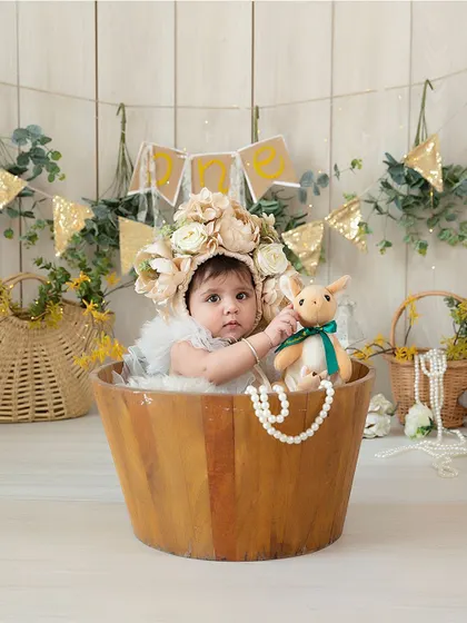 A cute portrait of a baby girl in a wooden bucket, holding her little toy. This sitter session captures her curiosity and adorable personality.