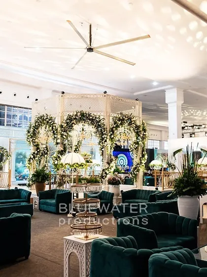 A wide view of the guest lounge at the 'Blue Palace' reception, featuring plush teal velvet sofas and unique floral installations.