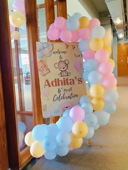 A welcome board for a 6-month celebration with a teddy bear theme. The C-shaped balloon arrangement in pastel colors frames the sign beautifully.