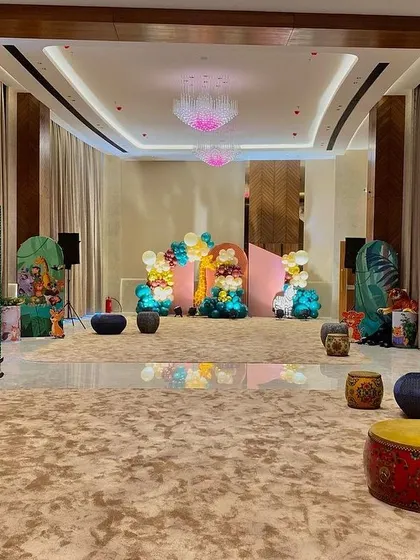 A wide view of a spacious hall decorated for a jungle theme, with green sequin walls, animal props, and low seating arrangements for a kid-friendly party.