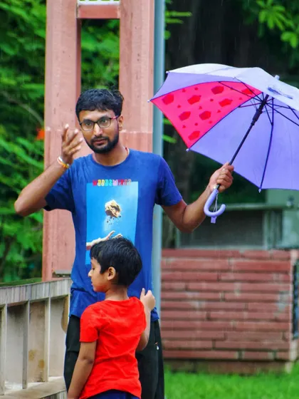 The father and son duo enjoying the rain. The father gestures while holding the umbrella, sharing a moment with his child during a walk in the park.
