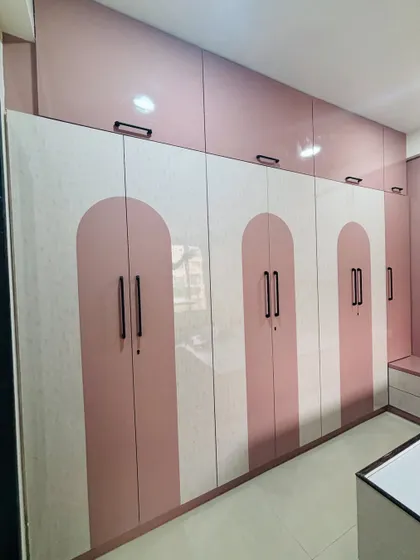 This large wardrobe uses a combination of pink and a textured white laminate with an arch pattern, creating a soft and elegant look.