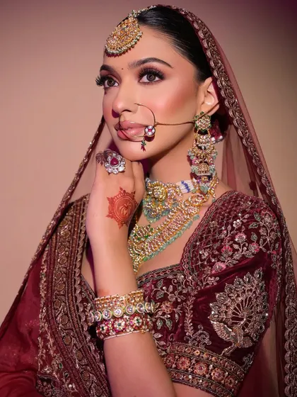 A modern bride in a traditional velvet lehenga. This look features a stunning red shimmer on the eyes, a flawless matte base, and bold jewellery for a truly royal feel.