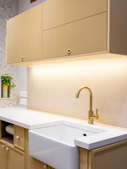 The fluted details on the upper cabinets in this kitchen add a beautiful, rhythmic texture. Paired with a farmhouse sink and brass faucet, the space feels warm, contemporary, and full of quiet character.