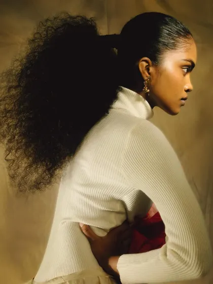 A profile portrait from the 'ANAINA' series, with soft light highlighting the model's features and voluminous ponytail. The image is serene and elegant.