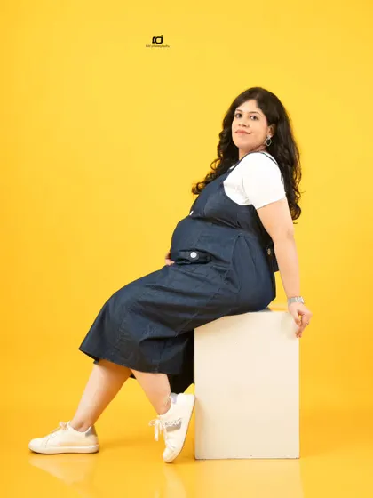 A modern and casual solo maternity portrait. The denim overalls and bright yellow background create a fun, fresh, and youthful vibe.