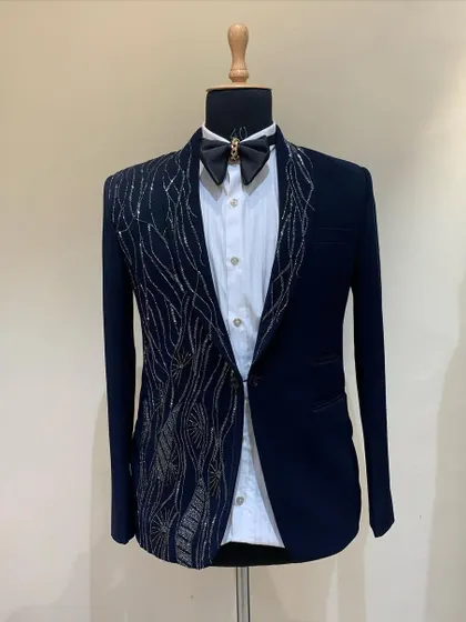 A navy blue tuxedo on display, featuring abstract silver and gold hand-embroidery that flows down one side of the jacket. This is an artistic piece for a client looking for something beyond a traditional tux.