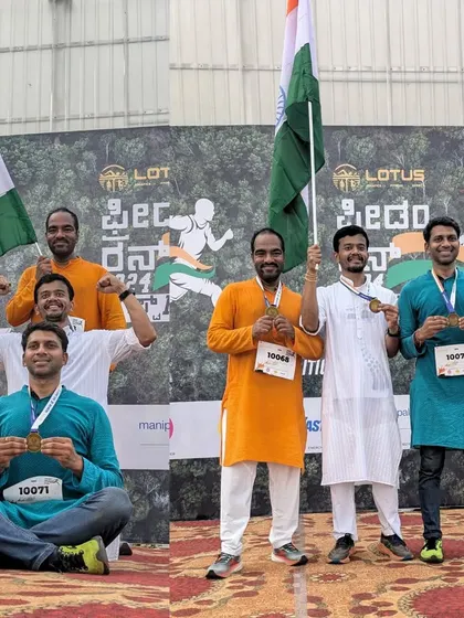 A group of runners in traditional attire celebrates their successful run with medals and flags.
