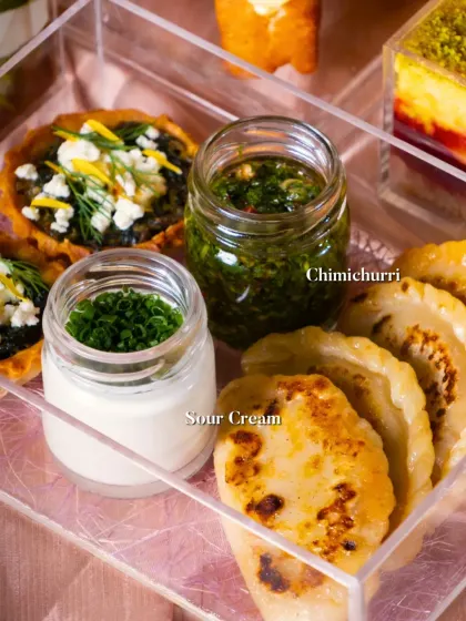 A festive platter featuring mini quiches and empanadas, served with fresh chimichurri and sour cream for dipping.