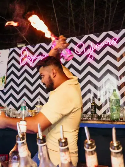 A bartender simultaneously pours a drink and handles a flaming bottle, showcasing the multitasking and skill involved in professional flair bartending.