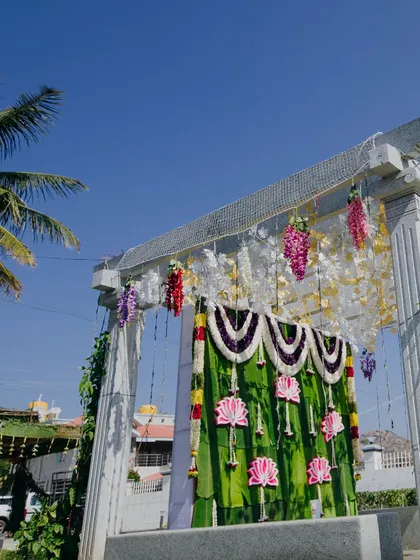 A simple yet beautiful decor setup at a temple entrance. The banana leaf backdrop with lotus cutouts and hanging floral strings creates a serene and auspicious atmosphere.