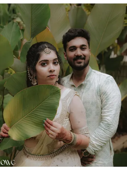 A creative portrait of a couple using a large leaf, blending them into the natural, green surroundings of their pre-wedding location.