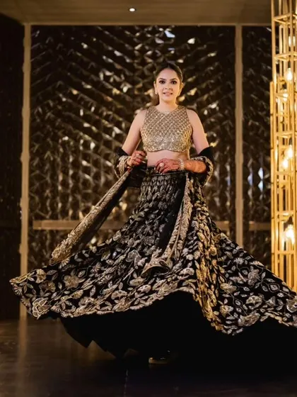 The bride poses in the golden entrance tunnel, her black and gold lehenga perfectly matching the decor.