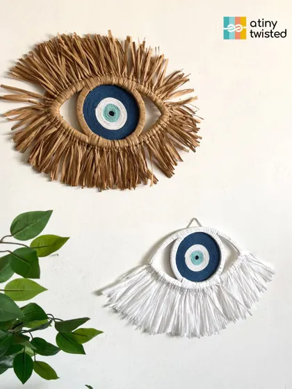 A closer look at my two evil eye designs. One is made with natural, earthy raffia, and the other with soft, white cotton fringe. Both are designed to be beautiful protectors for your space.