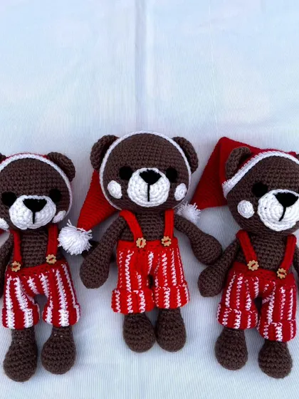 A trio of festive teddy bears dressed in Santa hats and striped overalls, ready for the Christmas season.