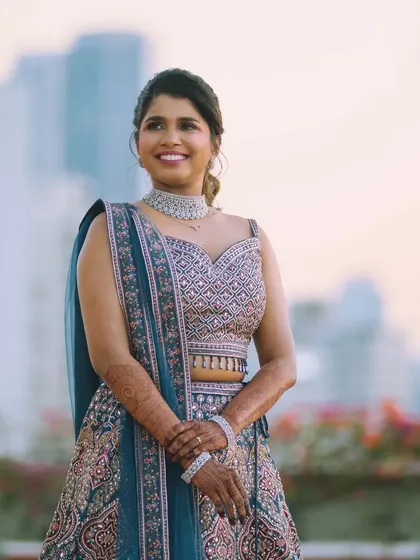 A stunning outdoor shot of the bride against the city skyline. Her blue and pink lehenga is paired with a fresh, glowing makeup look perfect for an evening reception.