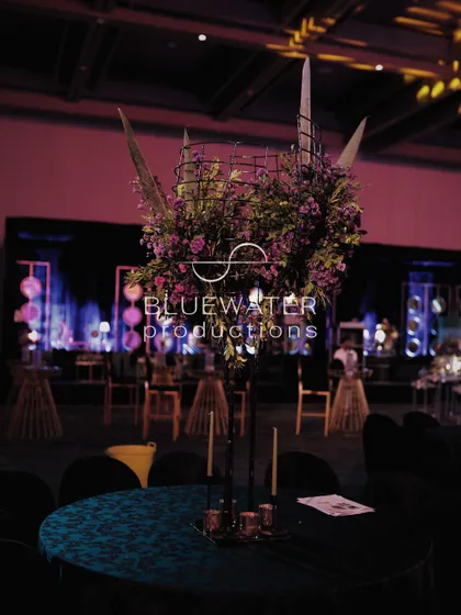 A tall centerpiece on a cocktail table, featuring a mix of florals and foliage in a dark, moody palette.